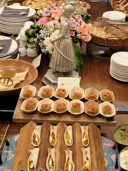 A closer view of the high-tea table, showing the variety of dishes like tacos, sandwiches, and hot entrees. The floral centerpiece adds a touch of elegance to the spread.