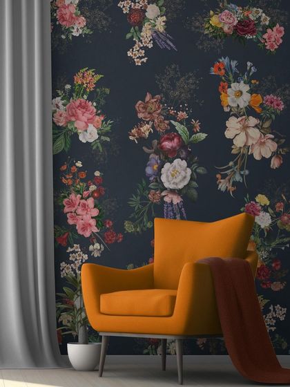 The floral wallpaper used as a feature wall behind a bold orange armchair, demonstrating how it can complement contemporary furniture.
