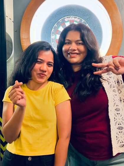 Two friends posing by the dartboard, showing off the fun and games that complement our karaoke nights. in the background.