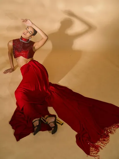 A high-fashion, artistic shot from the 'Scarlet Edit'. The overhead angle and dramatic pose create a visually interesting image that highlights the long train of the red skirt.