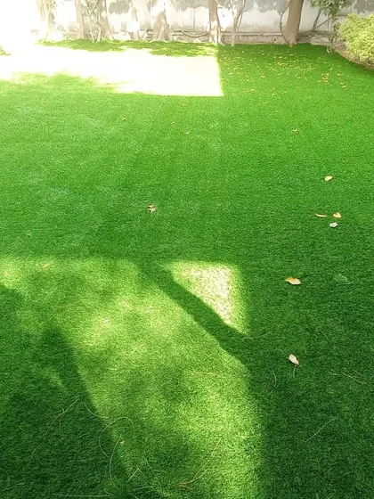 A ground-level view of a residential lawn installation. The artificial grass looks incredibly realistic under the bright sun, and it eliminates any issues with mud or uneven growth.