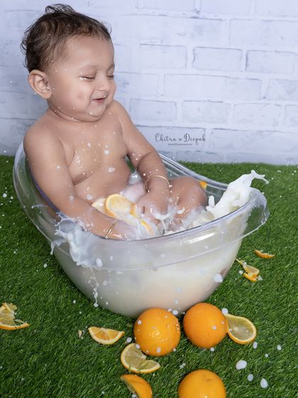 A joyful baby splashes happily in a milk bath filled with fresh orange slices, capturing a moment of pure, uninhibited fun.