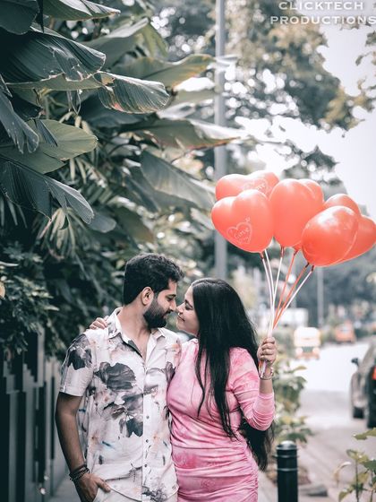A romantic pre-wedding photo of a couple on a city street, holding a bunch of heart-shaped balloons.