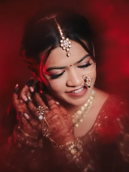A close-up portrait of the bride in her deep red wedding lehenga. The makeup features a soft smokey eye and a natural lip, creating a look that is both classic and modern.