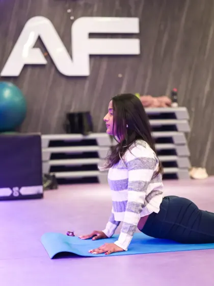 A member holds the Cobra Pose (Bhujangasana) on her blue mat. This classic yoga posture is excellent for strengthening the spine and opening the chest, and this photo captures the form and focus required.
