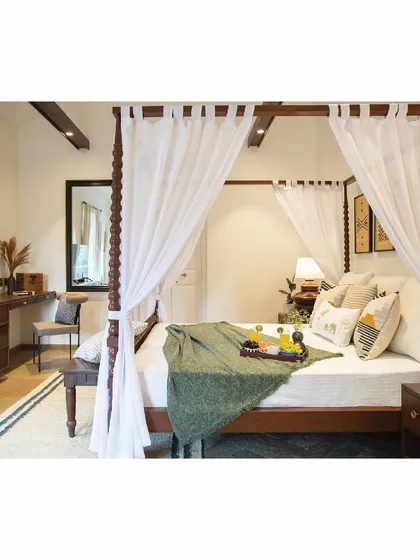 The dreamy master bedroom in our Goa project, featuring a four-poster bed draped with soft, buttery curtains. The tropical theme is carried through with a cool color palette and natural textures, creating a serene and romantic atmosphere.