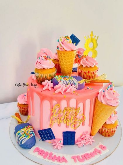 This drip cake is a party in itself. A vibrant pink base with a matching drip is loaded with treats like cupcakes, ice cream cones, chocolate bars, and sprinkles, making it perfect for a fun-filled birthday.