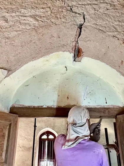 A worker inspects a crack in the vaulted ceiling. Identifying and repairing structural issues like this is a critical first step in any conservation project, ensuring the building's stability.