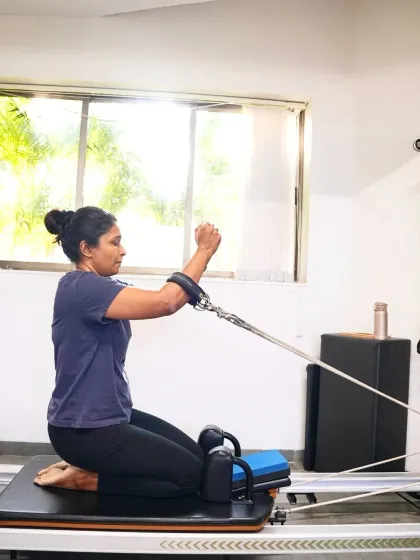 A kneeling arm exercise on the reformer challenges core stability while targeting the shoulders and back. This client maintains a strong, neutral spine, demonstrating excellent body awareness.
