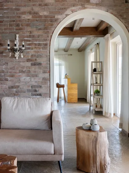 The living room's exposed brick wall is complemented by a classic candelabra-style wall sconce. An archway leads to the bar area, creating a sense of discovery and flow between spaces.