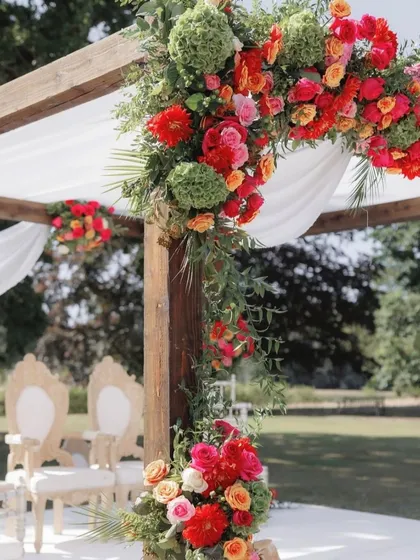 A detailed shot of a rustic wooden mandap, showcasing the vibrant floral arrangement. We used a mix of red, orange, and pink roses with fresh green foliage to create a rich and colorful corner piece.
