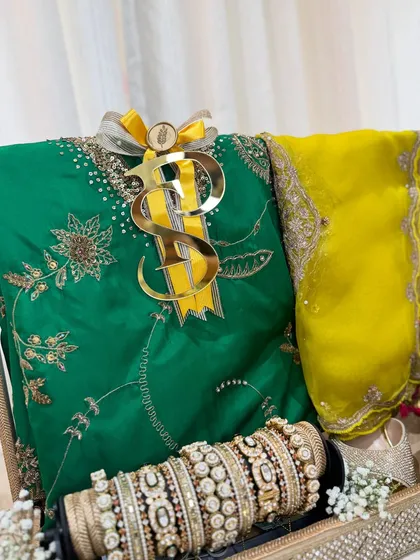 An emerald green and bright yellow outfit, complete with a set of traditional bridal bangles. The personalized initials add a modern, bespoke touch.