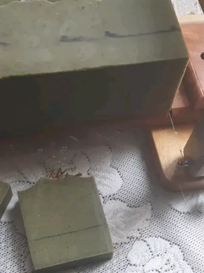The process of cutting the Moringa Mahua Butter soap loaf. You can see the rich, green color from the moringa leaves and the solid, dense texture of the finished bar.