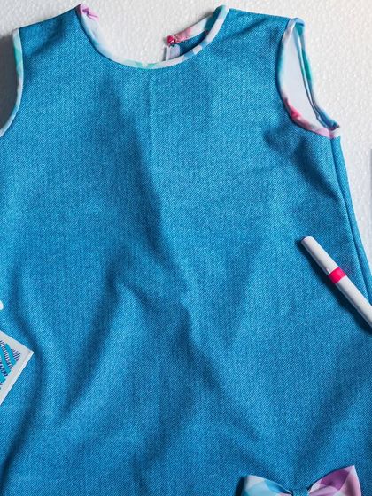 A top-down view of the denim and check dress, highlighting the clean lines and simple, sleeveless design that's perfect for warm weather.