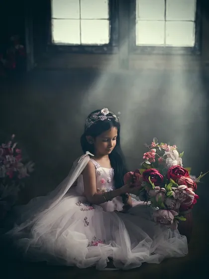 This is an example of our painterly portrait style, where we use dramatic lighting to create a soulful, artistic image. The soft light from the window illuminates this young girl in her princess gown, transforming a simple moment into a timeless piece of art.