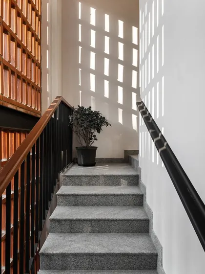 The brick jaali screen seen from the interior stairwell. Throughout the day, sunlight filters through the perforations, casting a dynamic pattern of light and shadow onto the white walls.