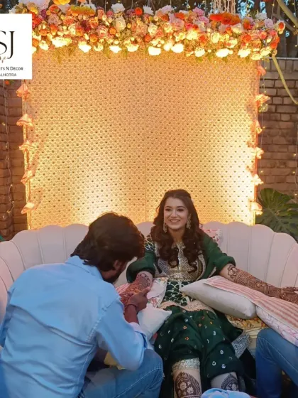 An elegant backdrop for a Mehendi ceremony. The bride enjoys her henna application in a beautifully decorated space with a floral and light-up backdrop designed by our team.