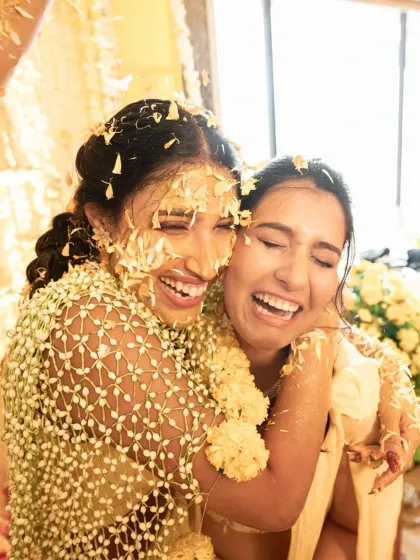 A heartfelt hug between the bride and her sister, both covered in haldi and flowers. A beautiful, emotional moment amidst the fun.