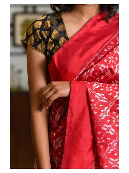 A close-up detail shot focusing on the red saree's fabric and the contrasting black and gold blouse. This type of image is crucial for showing product quality and craftsmanship online.