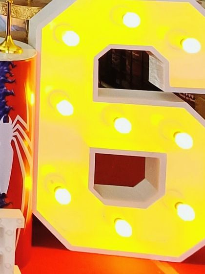 A close-up of a large, bright yellow light-up marquee number '6', perfect for a Spiderman or other superhero-themed birthday party.