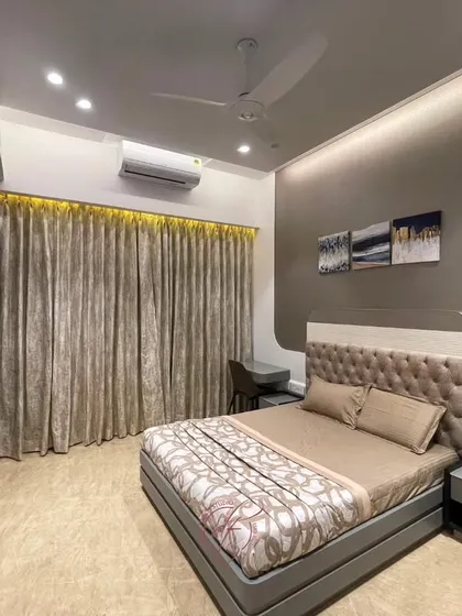 This bedroom features a plush, tufted headboard and a dedicated study nook by the window. The design is perfect for modern living, combining a restful space with a functional work area.