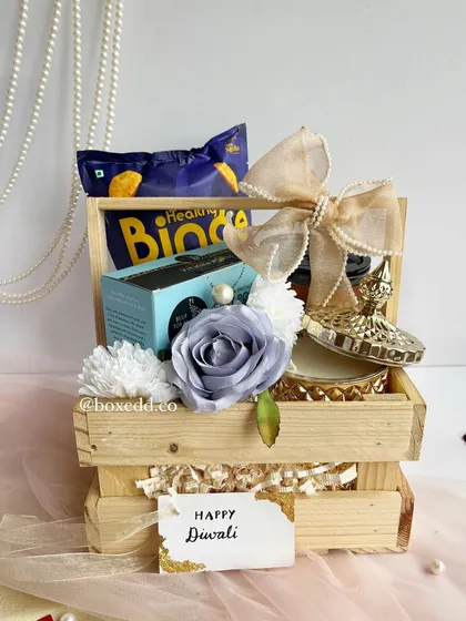 A unique wooden crate hamper for Diwali, adorned with a delicate blue rose. This gift combines snacks and decorative items, offering a fresh and appealing alternative to traditional gifts.