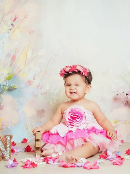 A joyful first birthday photo. This little one is all smiles surrounded by flowers and her 'ONE' sign.