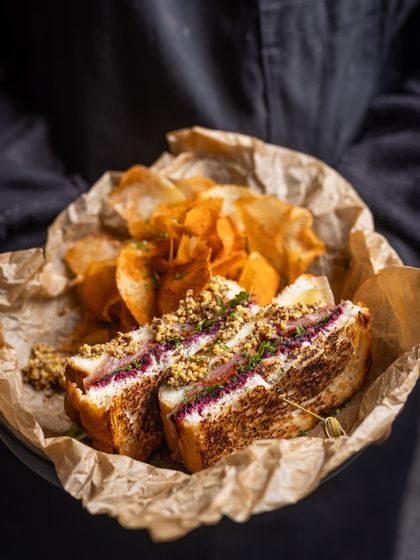 A delightful Ham and Cheese sandwich, perfectly grilled and served with a side of house-made chips. It’s a classic done right, ideal for a satisfying and delicious breakfast.