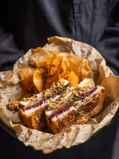 A delightful Ham and Cheese sandwich, perfectly grilled and served with a side of house-made chips. It’s a classic done right, ideal for a satisfying and delicious breakfast.