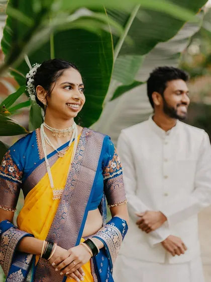 A lovely portrait of the bride in her colorful Paithani saree, with her partner smiling in the background.
