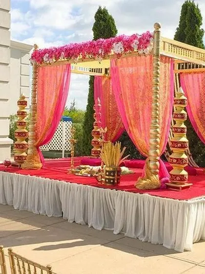 An outdoor wedding mandap designed with vibrant pink and gold drapes. This setup is perfect for a daytime ceremony, combining the richness of traditional colors with the beauty of a natural setting.