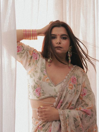 A full look featuring a delicate floral saree. The makeup is soft and romantic, with a focus on a flawless base and defined eyes that complement the colors of the outfit without overpowering it.