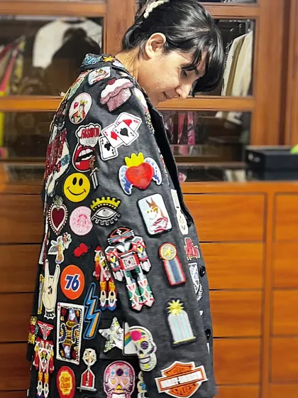 A closer look at the detailed patch and embroidery work on the custom trench coat. Each patch, from the sacred heart to the smiley face and playing cards, was chosen and placed to build a rich visual narrative.