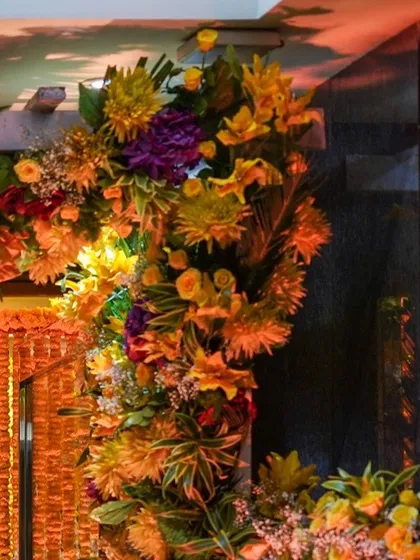 The side of a floral arch, showcasing the variety of flowers and greenery used to create a full and luxurious feel. The warm lighting enhances the golden tones of the decor.