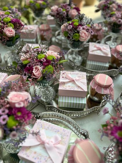 An elegant display of our party favours, featuring small gift boxes and cookie jars on silver trays with fresh floral arrangements.