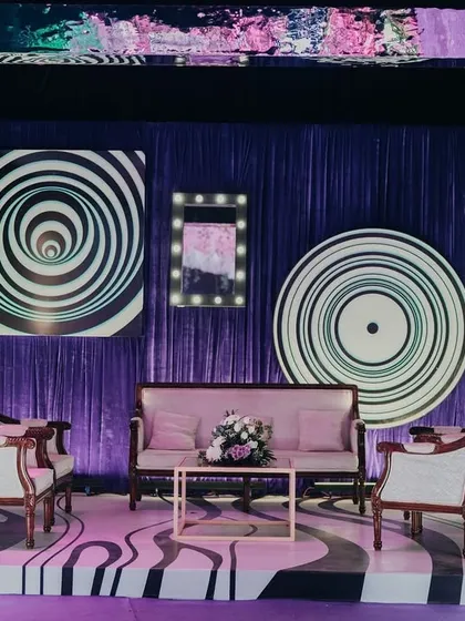 A unique photo booth designed with hypnotic spiral patterns and a purple-draped background. The vintage-style furniture provides a cool contrast to the modern, psychedelic visuals.