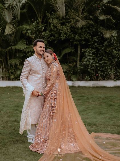 A full-length portrait of the couple, with the bride's stunning lehenga and long veil creating a dramatic and beautiful silhouette.