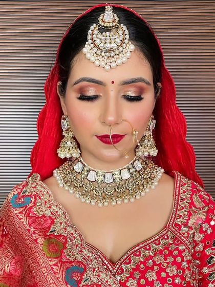 A bride with a red dupatta wearing a white and gold Kundan choker, matching jhumkas, and an oversized maang tikka. This is a classic combination for a traditional wedding ceremony.