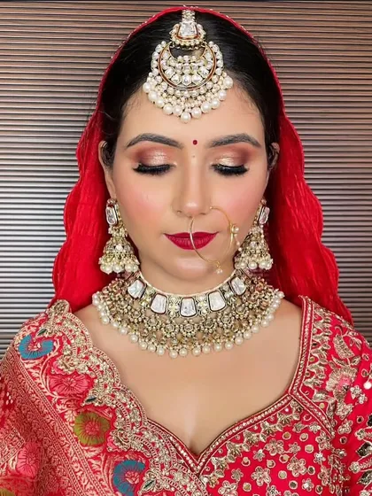 A bride with a red dupatta wearing a white and gold Kundan choker, matching jhumkas, and an oversized maang tikka. This is a classic combination for a traditional wedding ceremony.