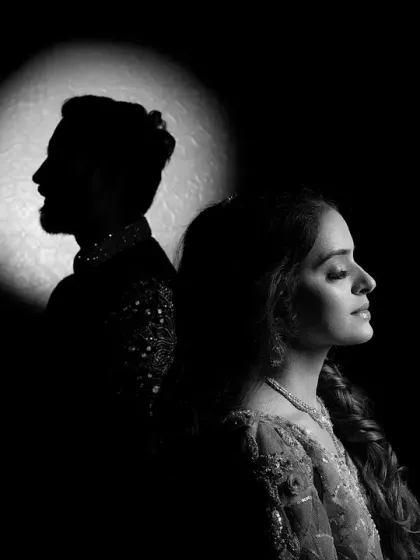 A dramatic black and white version of a spotlight portrait. The high contrast between light and shadow creates a powerful and cinematic feel, emphasizing the couple's silhouettes.