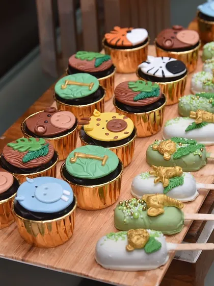 The details make the theme. This shot highlights the variety in the jungle dessert set, showing off the hippo, giraffe, and zebra cupcake toppers alongside the green and gold jungle-leaf cakesicles.