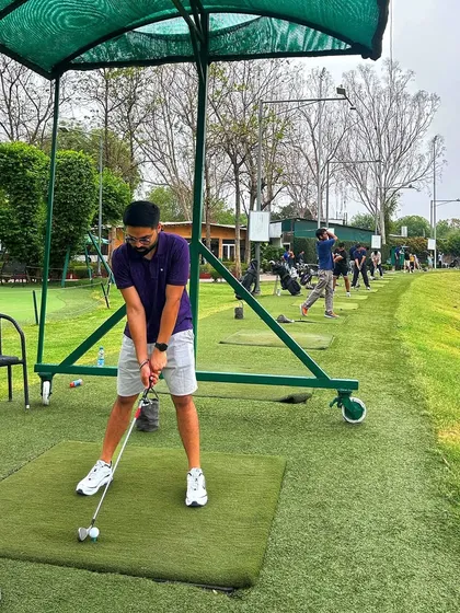A young golfer in a purple shirt takes a practice swing on the mat, fully focused on his form.