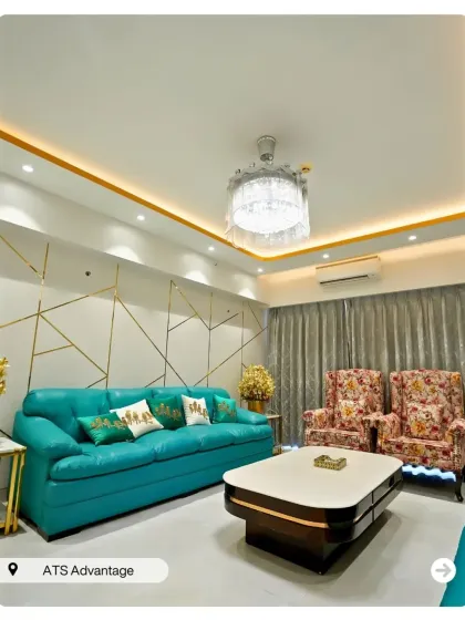 An eclectic living room design featuring a bold turquoise sofa and floral-patterned armchairs. The geometric gold-lined accent wall adds a modern, glamorous touch.