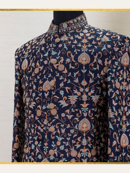 A close-up of a mannequin dressed in a navy sherwani with dense, multi-colored floral embroidery. This piece is a timeless masterpiece, telling a story of heritage and tradition through its threads.