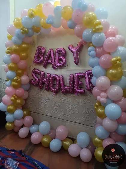 A simple and sweet baby shower arch. This home setup uses pink, blue, and gold balloons with "BABY SHOWER" foil letters to create a festive corner.