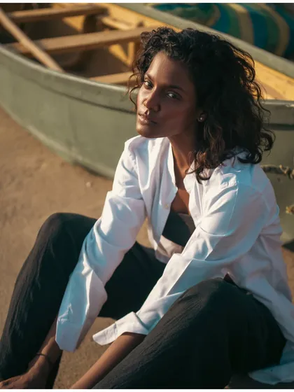 A beautiful, naturally lit portrait with a soft and thoughtful expression. The out-of-focus boat in the background adds to the coastal atmosphere.