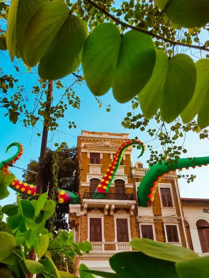 A whimsical installation of giant, colorful octopus tentacles emerging from the windows of a classic old building in Mumbai. A surreal and playful piece of public art.