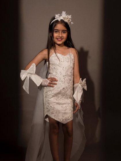 A glamorous white dress with a detachable tail, sequin details, and matching bow gloves for a complete party look.