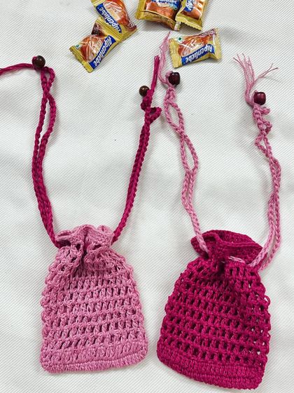 Two handmade crochet pouches in different shades of pink, one light and one dark. These are shown with small wooden beads on the drawstrings, adding a nice finishing touch.
