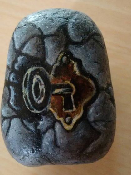 A pebble painted to look like an old, cracked stone wall with a rustic keyhole. These small pieces are fun to create and make for unique decorative items.